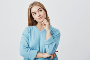 Face expressions and emotions. Thoughtful young pretty girl in blue sweater holding hand under her head, having doubtful look while can’t decide what clothes to wear on friend’s birthday party